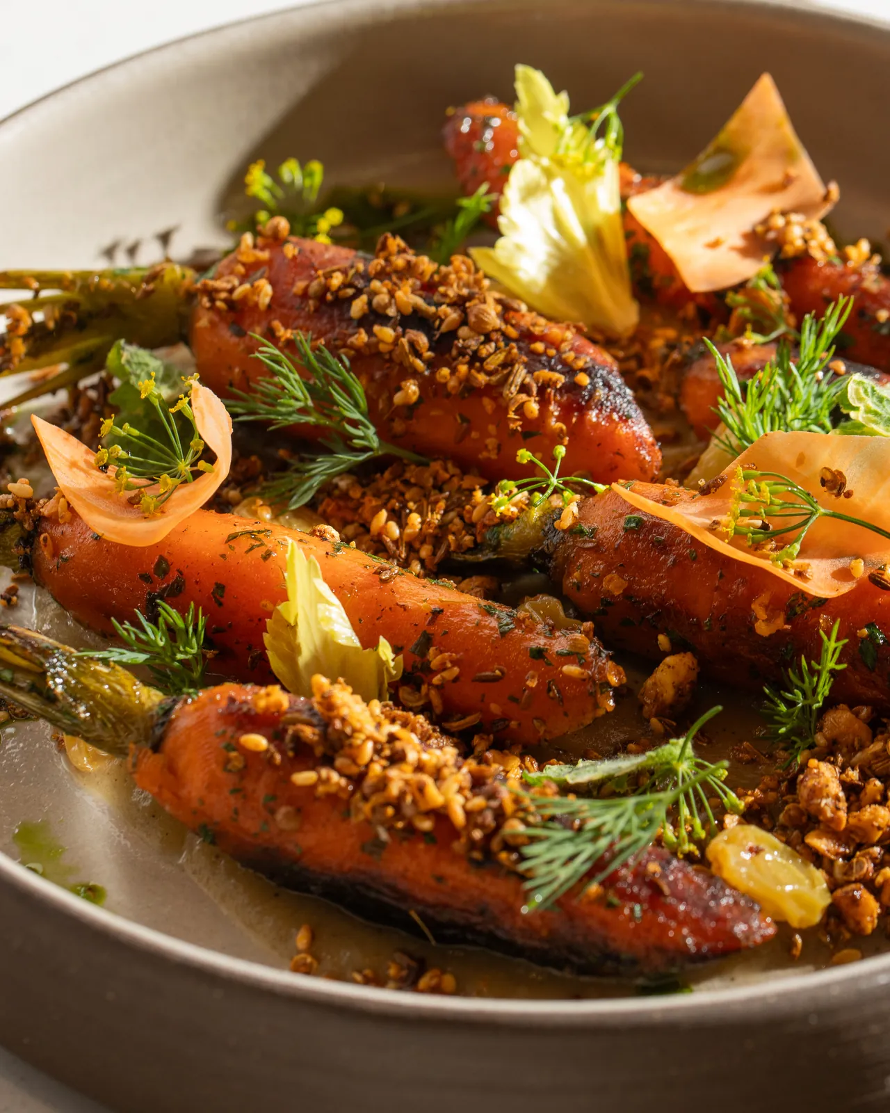 Roasted carrots under a golden crumble, with dill and thin, pale-orange shavings, in a grey bowl